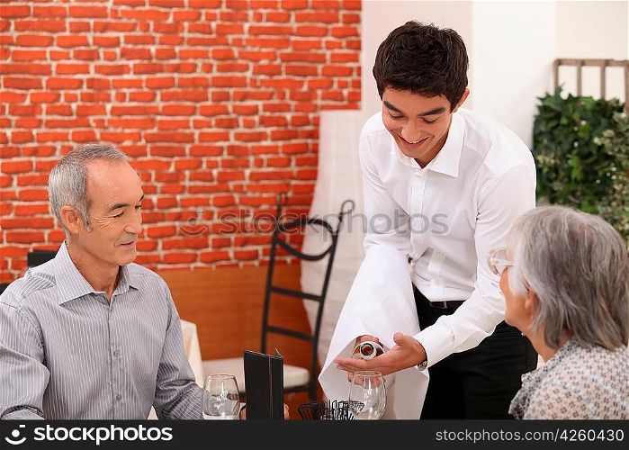 Young waiter pouring wine for an older couple
