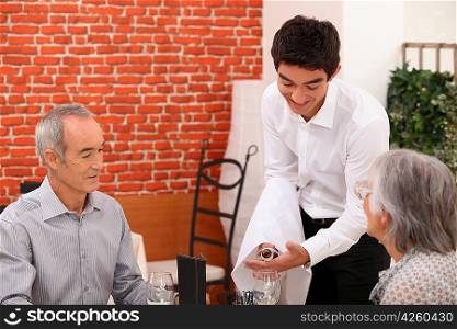 Young waiter pouring wine for an older couple