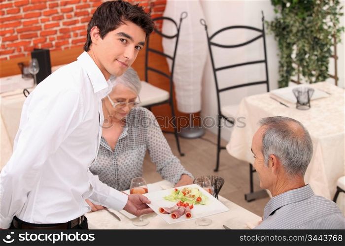 Young waiter serving senior couple in restaurant