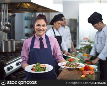 young waitress presenting dishes of tasty meals in commercial kitchen. young waitress showing dishes of tasty meals