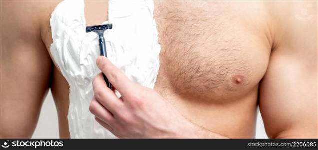 Young white man holds razor shaves his chest with white shaving foam on white background. Man shaving his torso. Young man shaving his chest