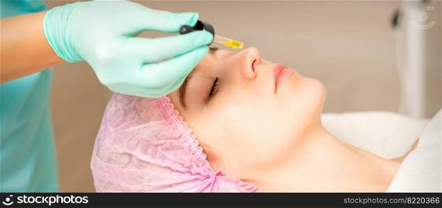 Young white woman getting acid organic retinol peel face skin with the pipette in a beauty clinic. Young white woman getting acid organic retinol peel face skin with the pipette in a beauty clinic.