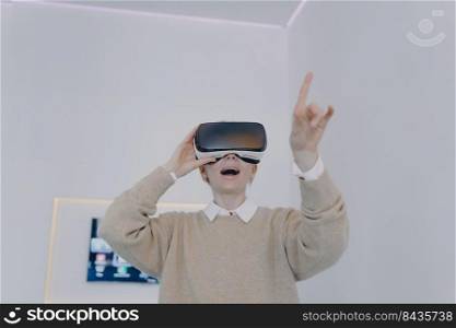 Young white woman in VR glasses in futuristic office. Girl in VR goggles is pointing with finger and looking into virtual reality. Business woman in 3d headset working on project in cyberspace.. Young white woman in VR glasses in futuristic office. Girl in VR goggles is pointing with finger.