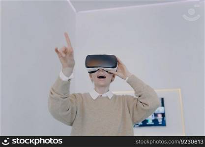 Young white woman in VR glasses in futuristic office. Girl in VR goggles is pointing with finger and looking into virtual reality. Business woman in 3d headset working on project in cyberspace.. Young white woman in VR glasses in futuristic office. Girl in VR goggles is pointing with finger.