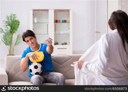 Young wife is trying to seduce husband from watching football an. Young wife is trying to seduce husband from watching football and tv. Young wife is trying to seduce husband from watching football an