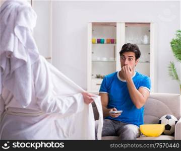 Young wife is trying to seduce husband from watching football and tv. Young wife is trying to seduce husband from watching football an
