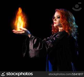Young witch girl holds fire isolated on black