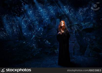 Young witch in night forest
