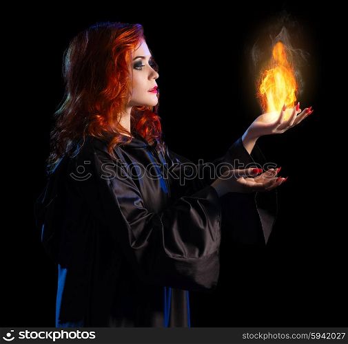 Young witch with flame isolated on black