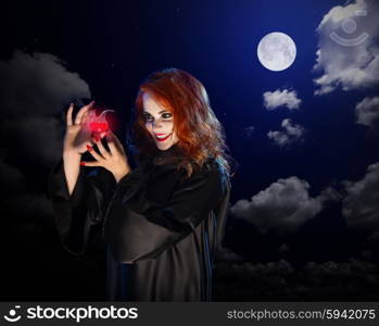 Young witch with red potion on night sky background