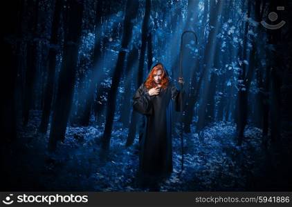 Young witch with staff in night forest