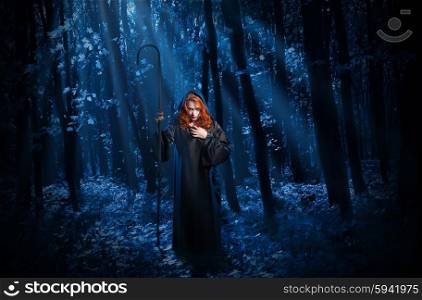 Young witch with staff in night forest