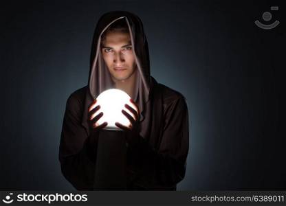 Young wizard with crystal ball in dark room