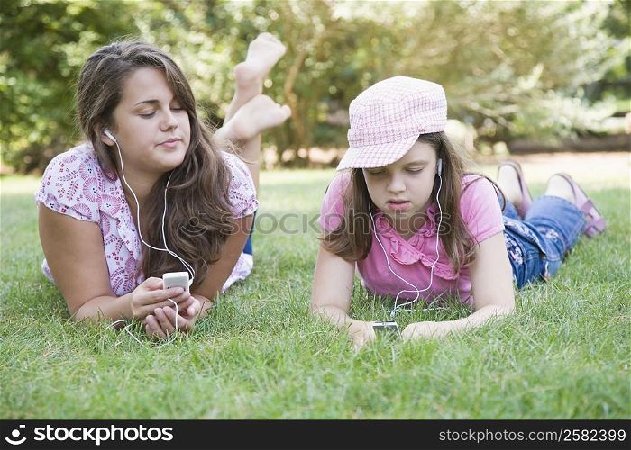 Young woman and a girl lying on grass in a park and listening to MP3 players