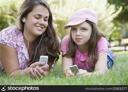 Young woman and a girl lying on grass in a park and listening to MP3 players
