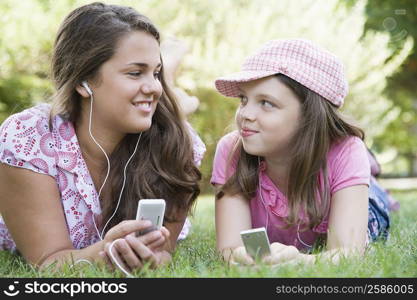 Young woman and a girl lying on grass in a park and listening to MP3 players