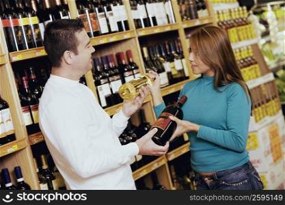 Young woman and a mid adult man looking at each other and holding wine bottles