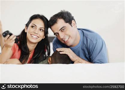 Young woman and a mid adult man lying down with their son on the bed and smiling