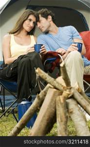 Young woman and a mid adult man sitting in front of a camping tent