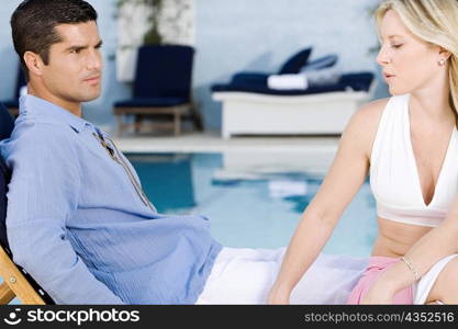 Young woman and a mid adult man sitting on a deck chair at the poolside