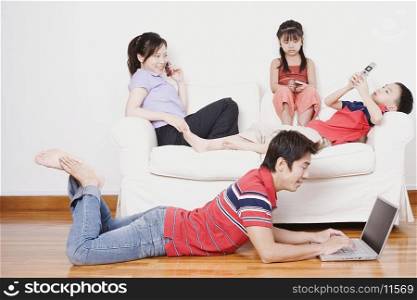 Young woman and her son and daughter sitting on a couch with a mid adult man lying on the floor with a laptop