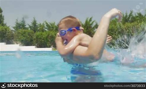 Young woman and little boy are having fun in their home pool, woman is lifting up the boy and drop him to water.