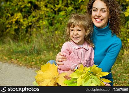 young woman and little girl laugh with leaves in hands in garden autumn
