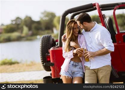 Young woman and man having fun outdoor near red car at hot summer day
