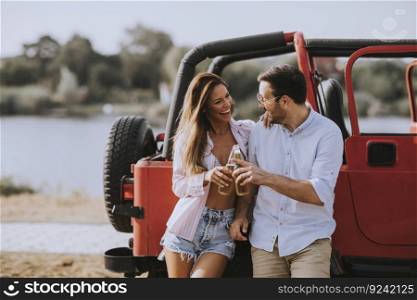 Young woman and man having fun outdoor near red car at hot summer day