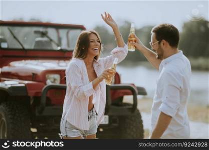 Young woman and man having fun outdoor near red car at summer day