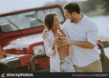 Young woman and man having fun outdoor near red car at summer day