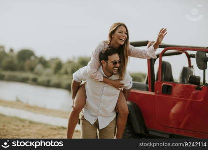 Young woman and man having fun outdoor near red convertible car at summer day