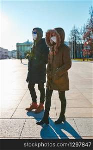 Young woman and man in the hoods wearing the face masks to avoid virus infection and to prevent the spread of disease. People walking in city centre. Virus infection protection. Real people, authentic situations