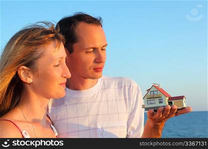 Young woman and man keeping in hands model of house with garage against sea in summer