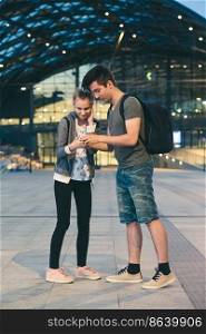 Young woman and man looking at screen of smartphone during walk in the city at night