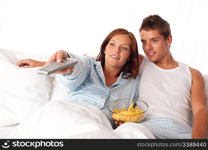 Young woman and man lying in bed watching television and eating crisps