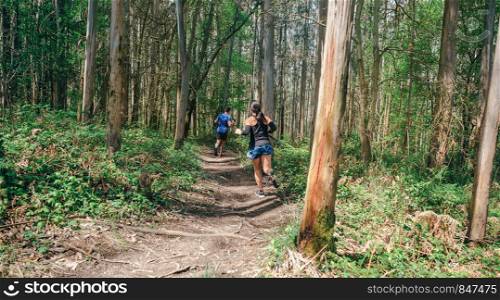 Young woman and man participating in a trail race through the forest. Young woman and man doing trail