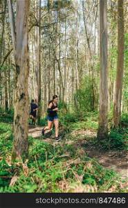 Young woman and man participating in a trail race through the forest. Young woman and man doing trail