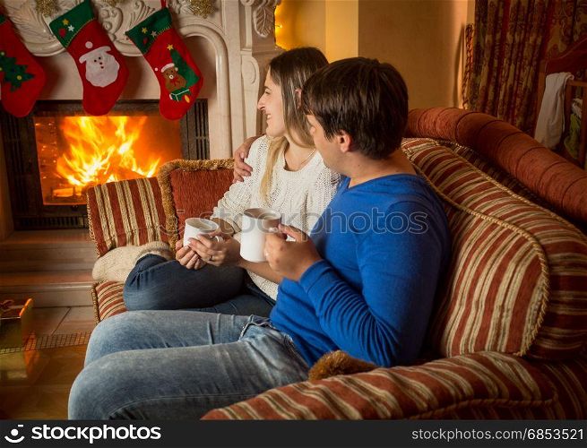 Young woman and man relaxing by the fireplace and decorated Christmas tree