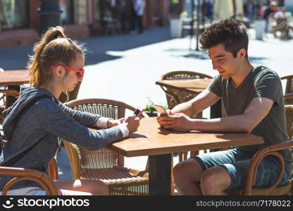 Young woman and man sitting in pavement cafe a the table talking and using mobile phones