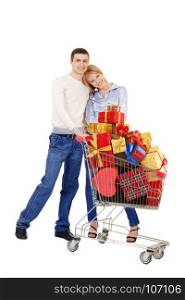 Young Woman and Man Standing Together Holding a Full Shopping Trolley with Red, Gold and Yellow Christmas Gifts isolated on White Background