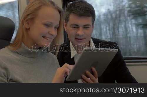 Young woman and man traveling by train. They talking and using tablet computer to entertain themselves during the ride