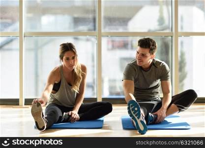 Young woman and man working out indoors. Two people streching their legs on the floor of a gym.