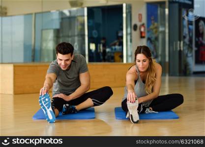 Young woman and man working out indoors. Two people streching their legs on the floor of a gym.