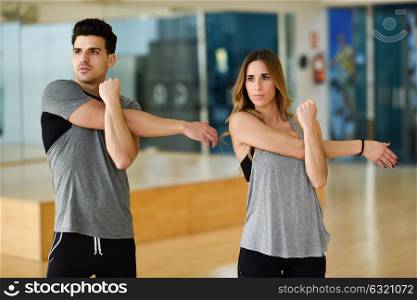 Young woman and man working out indoors. Two people stretching their arms in a gym.