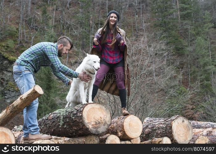 Young woman and men on wood logs in the forest. White dog