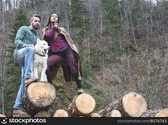 Young woman and men on wood logs in the forest. White dog