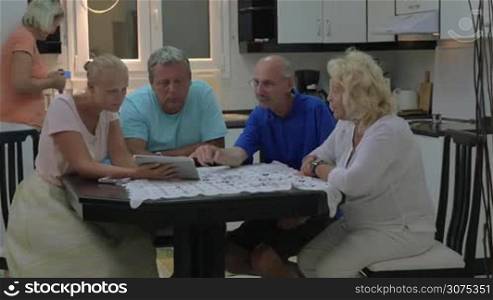 Young woman and senior people sitting at the table at home. Family members discussing something using tablet computer