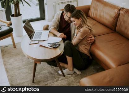 Young woman and young man using laptop while sitting by the sofa at home