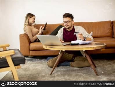 Young woman and young man using laptopfor online payment while sitting by the sofa at home